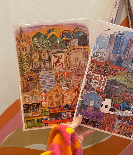 a hand holding two art prints. one of Fremantle and one of Perth