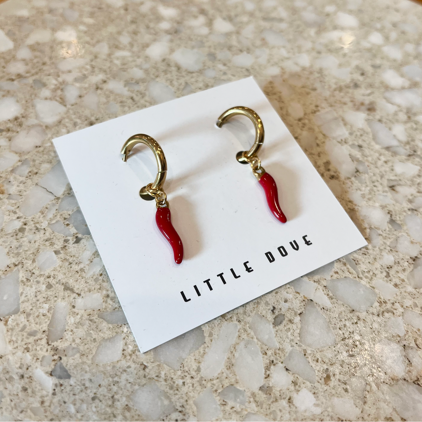 Pair of earrings on a 'Little Dove' branded card on a textured rock surface