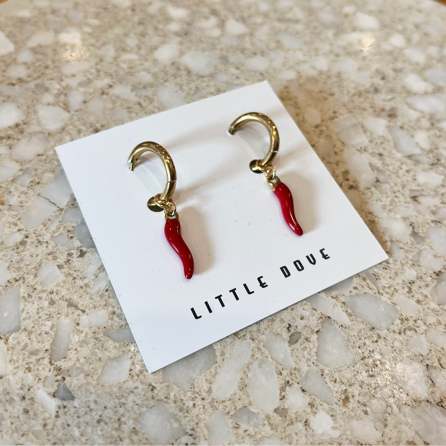 Pair of earrings on a 'Little Dove' branded card on a textured rock surface